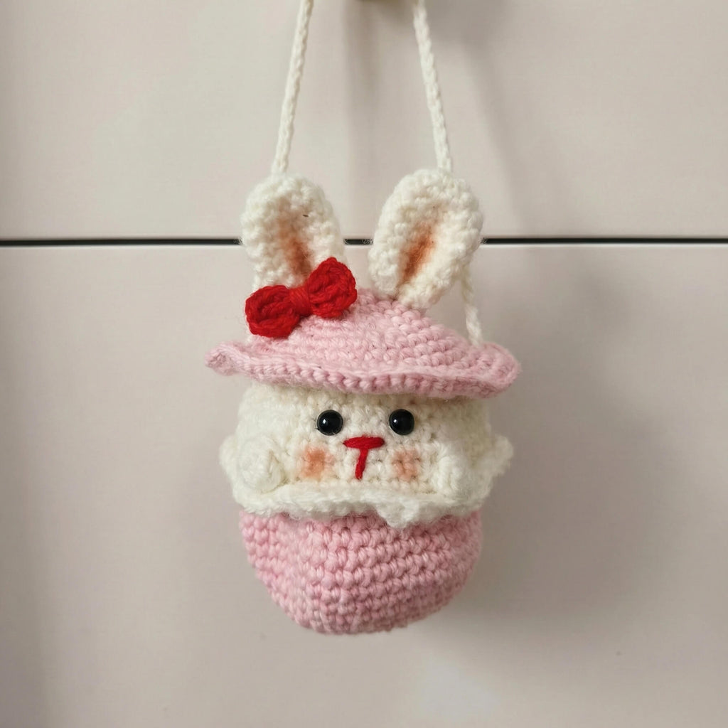 Crocheted bunny with a pink hat and red bow on a neutral background