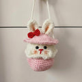 Crocheted bunny with a pink hat and red bow on a neutral background