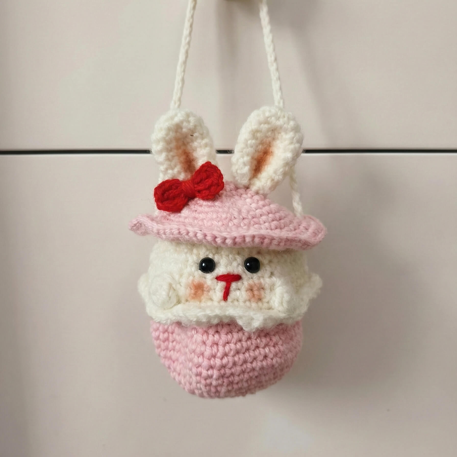 Crocheted bunny with a pink hat and red bow on a neutral background