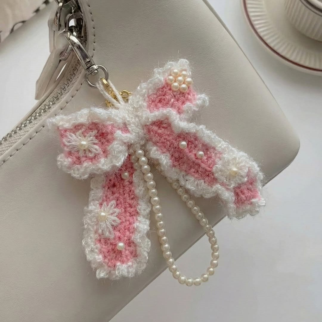 Pink and white crocheted bow keychain with pearls on a beige handbag.