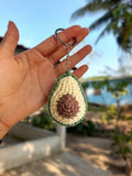 Hand holding a crocheted avocado keychain with a blurred outdoor background